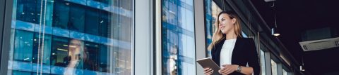 lady standing in building holding an iPad and looking out the window