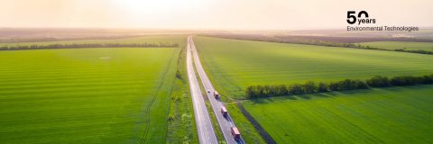 Cars and trucks on country road between green fields