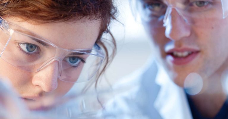 Two young scientists wearing safety goggle look closely at an object out of shot